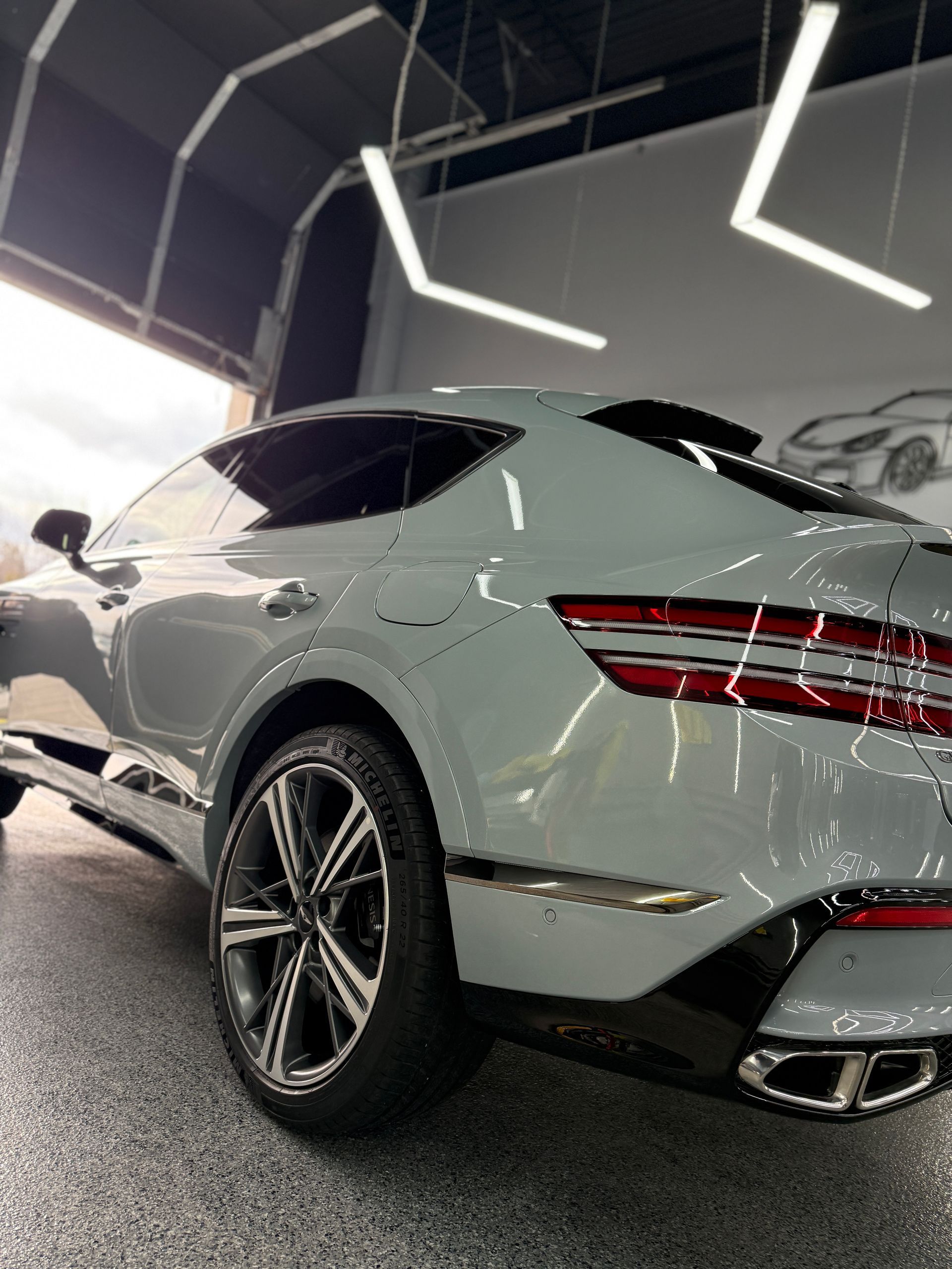 A low-angle view of a grey Genesis GV80 Coupe parked inside a garage with bright modern lighting.