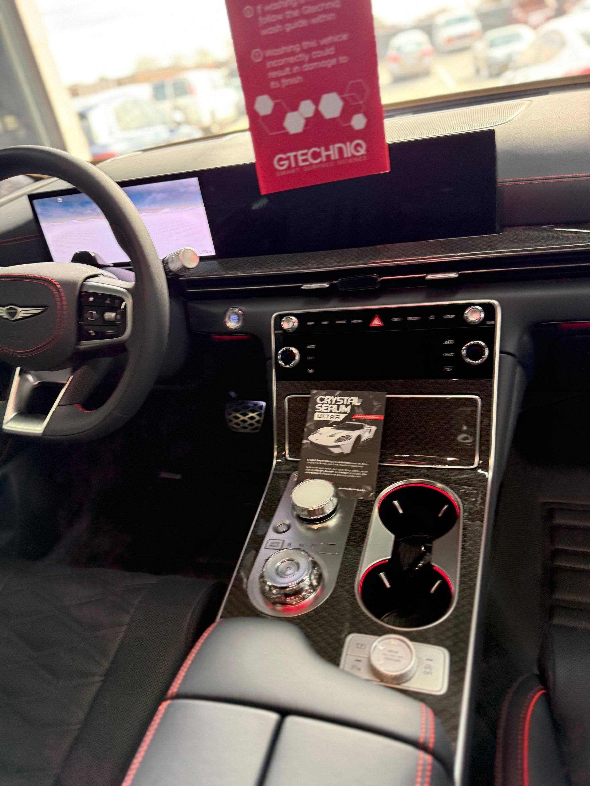 The interior of a modern Genesis car with a digital dashboard, leather steering wheel, and a center console with dial controls.