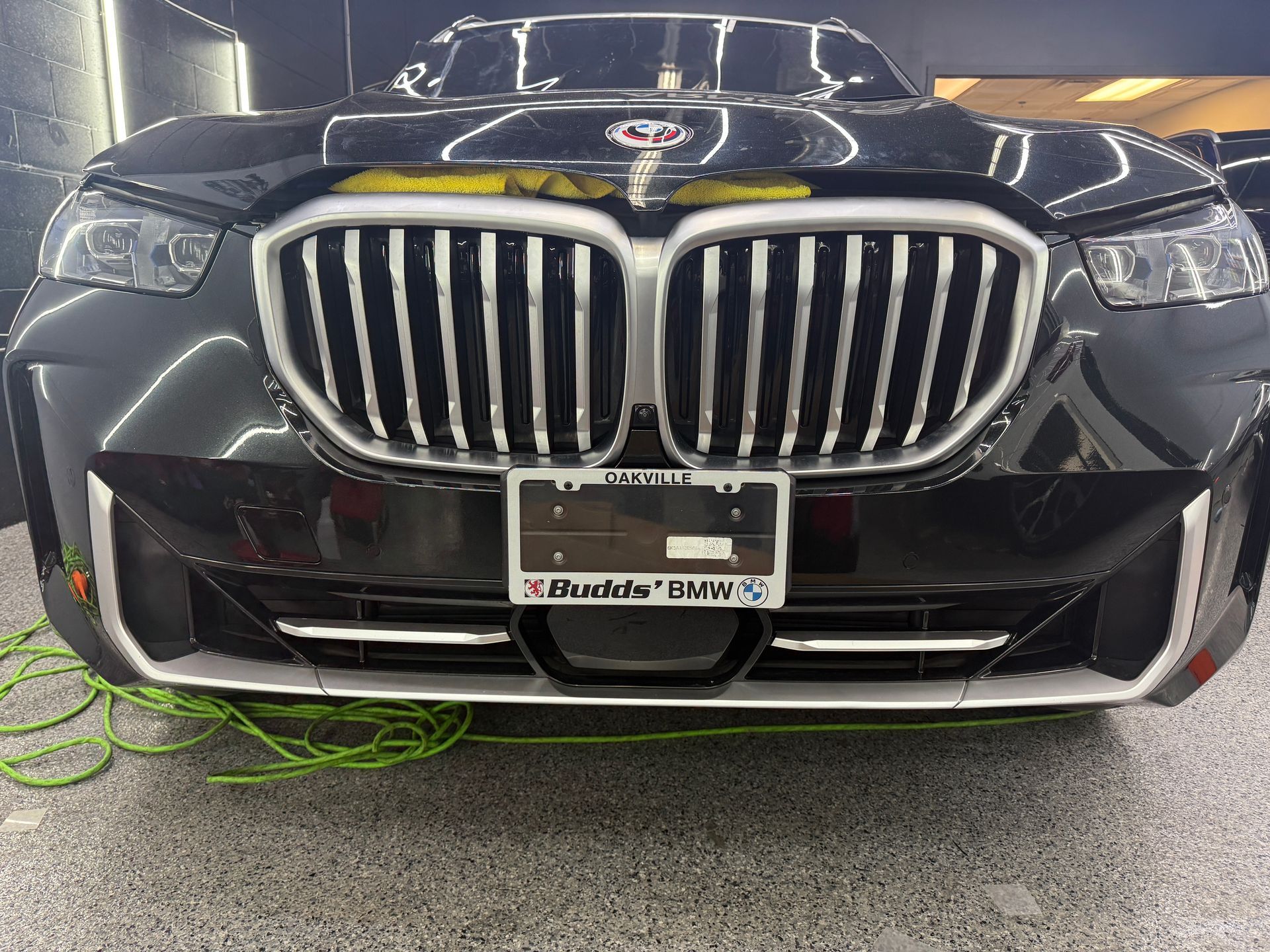 Front view of a shiny black BMW SUV with a silver grille and a dealership license plate frame in a garage setting.