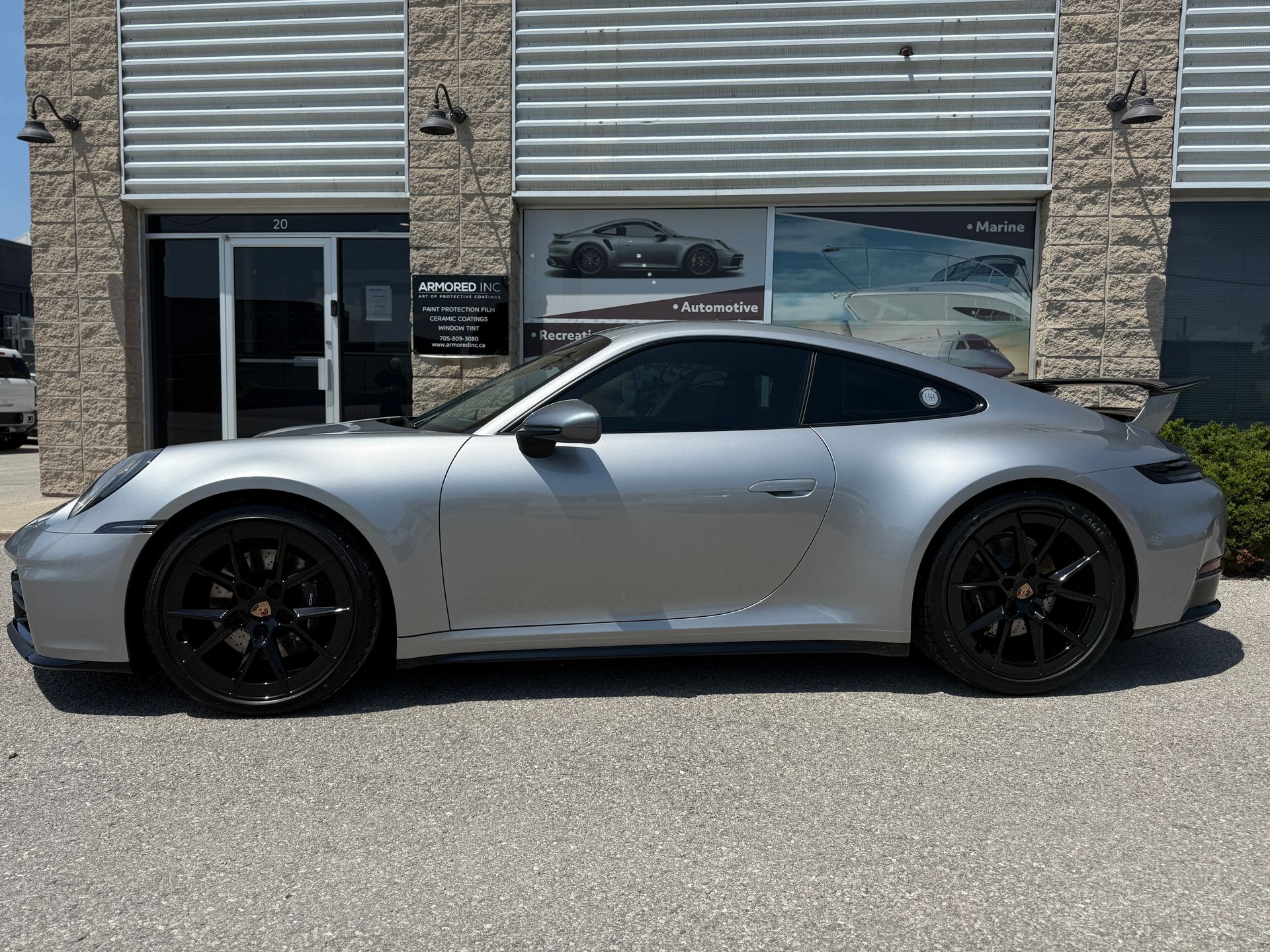 A silver Porsche sports car parked in front of a building with a gray facade on a sunny day.