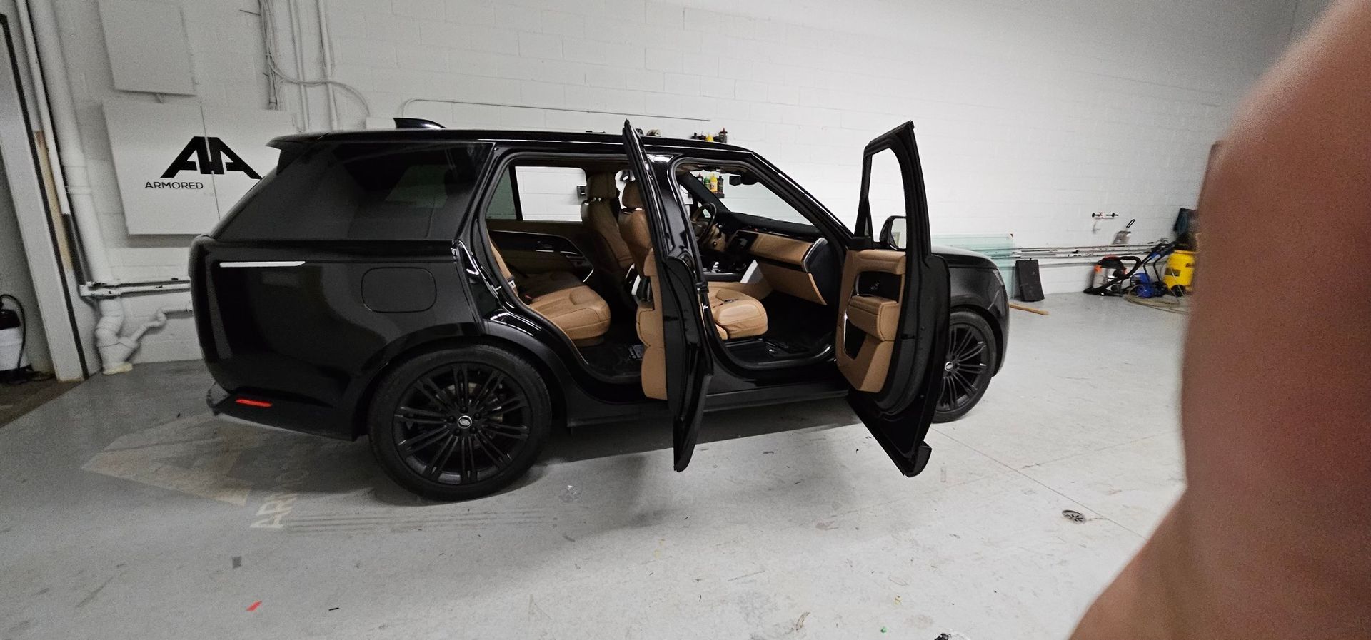 Black luxury SUV with doors open, showcasing a tan leather interior, parked inside a spacious, well-lit garage.