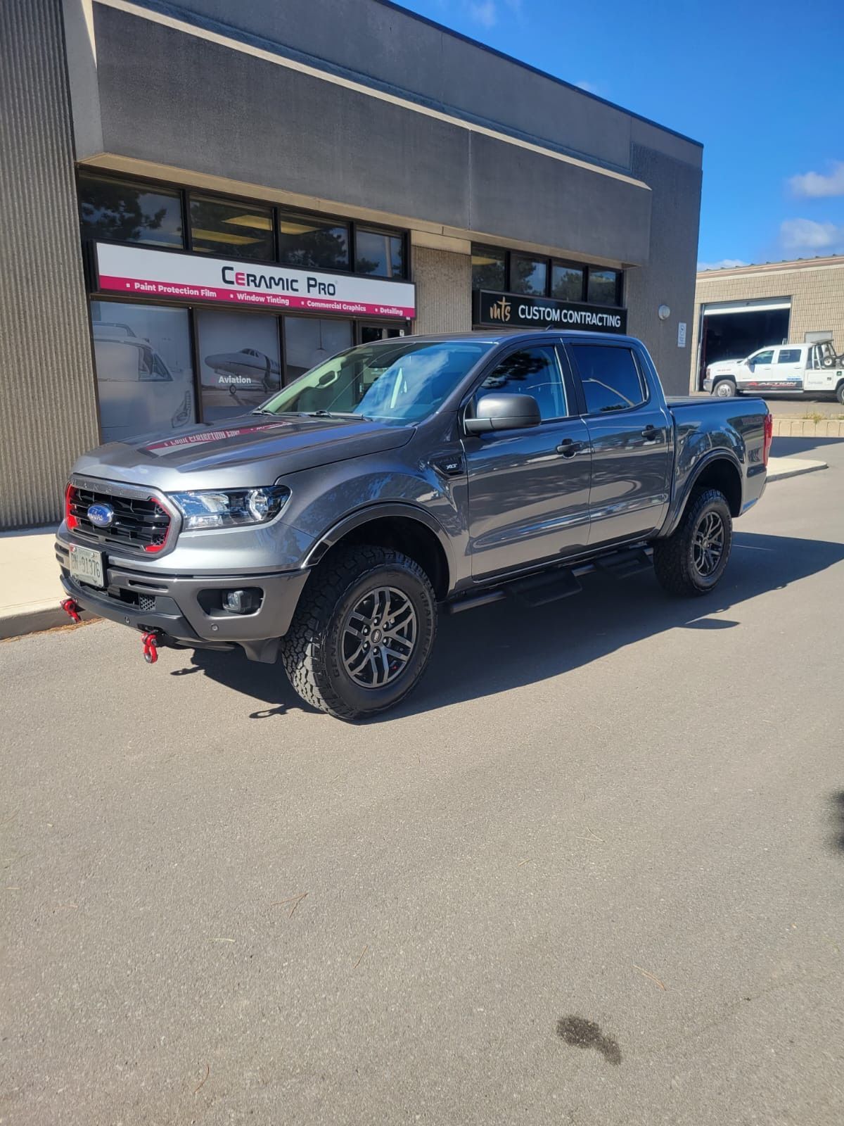A grey Ford Ranger pickup truck parked in front of a building with a red sign.