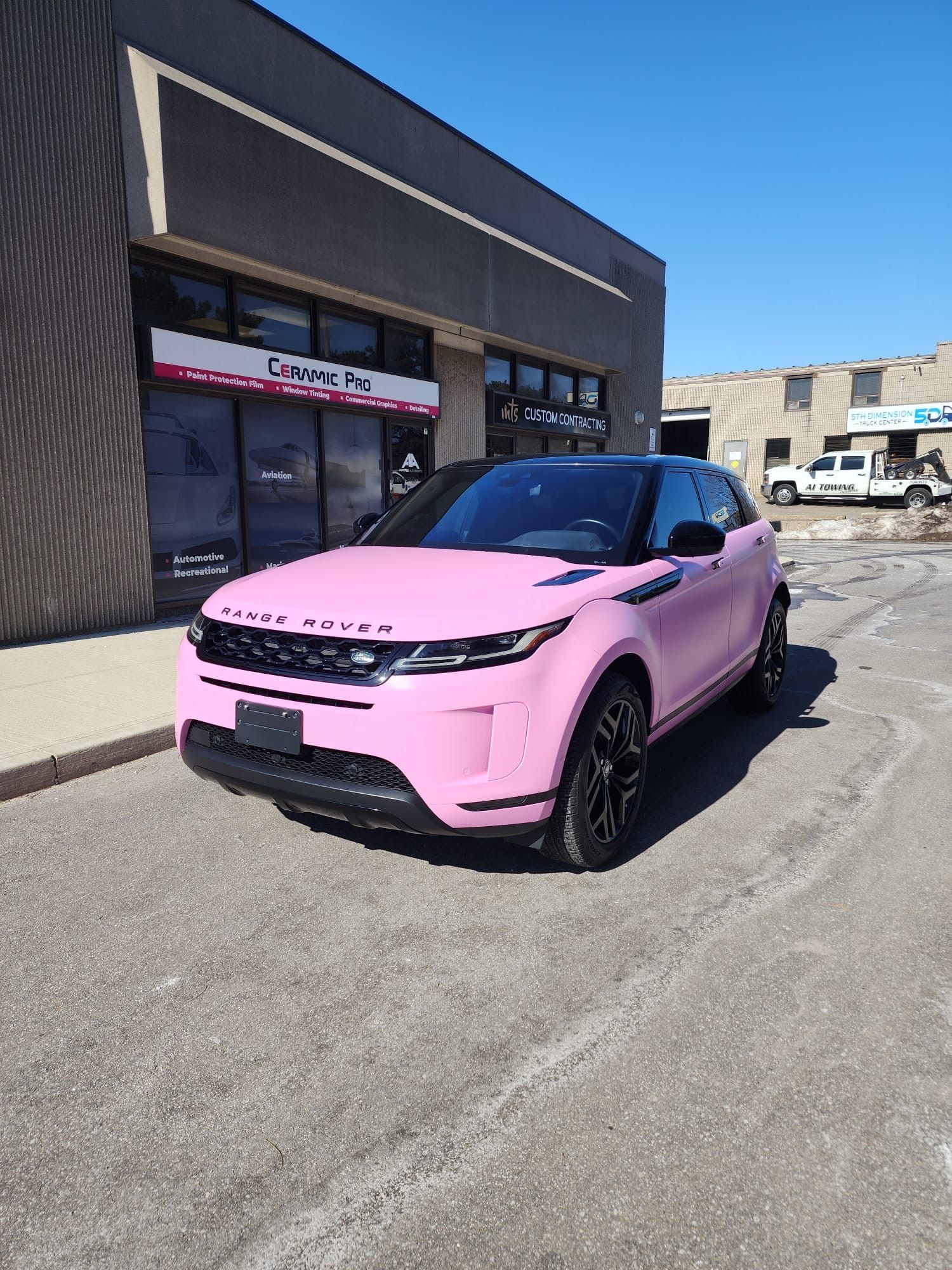 A matte light pink Range Rover parked in front of a commercial building on a sunny day.