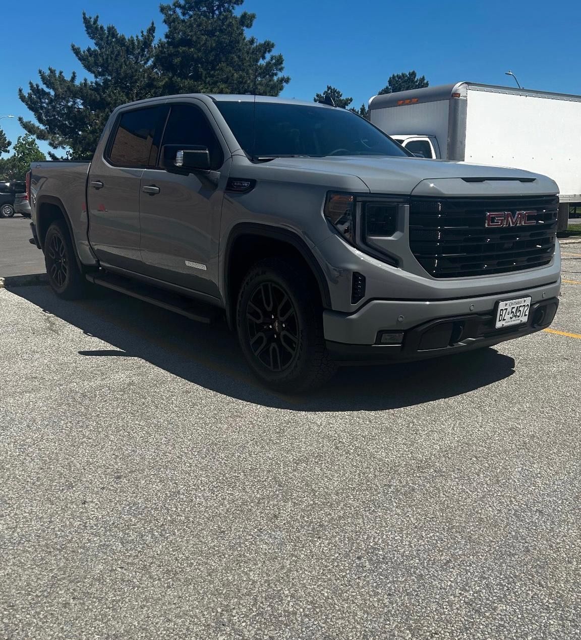 A gray GMC Sierra pickup truck parked on a gravel lot under a clear blue sky.