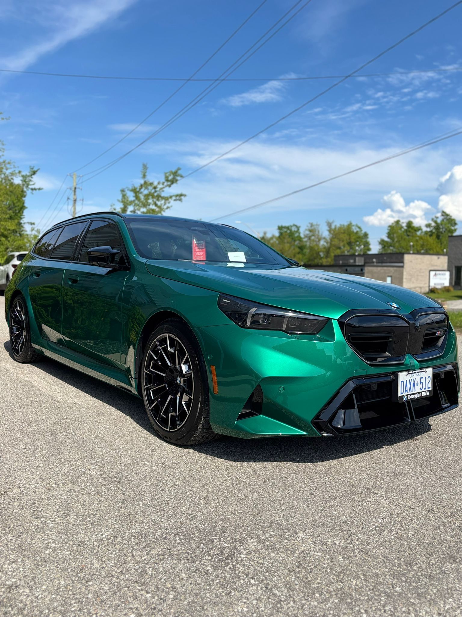 A metallic green sedan with black accents and wheels parked on a gravel lot under a bright blue sky.