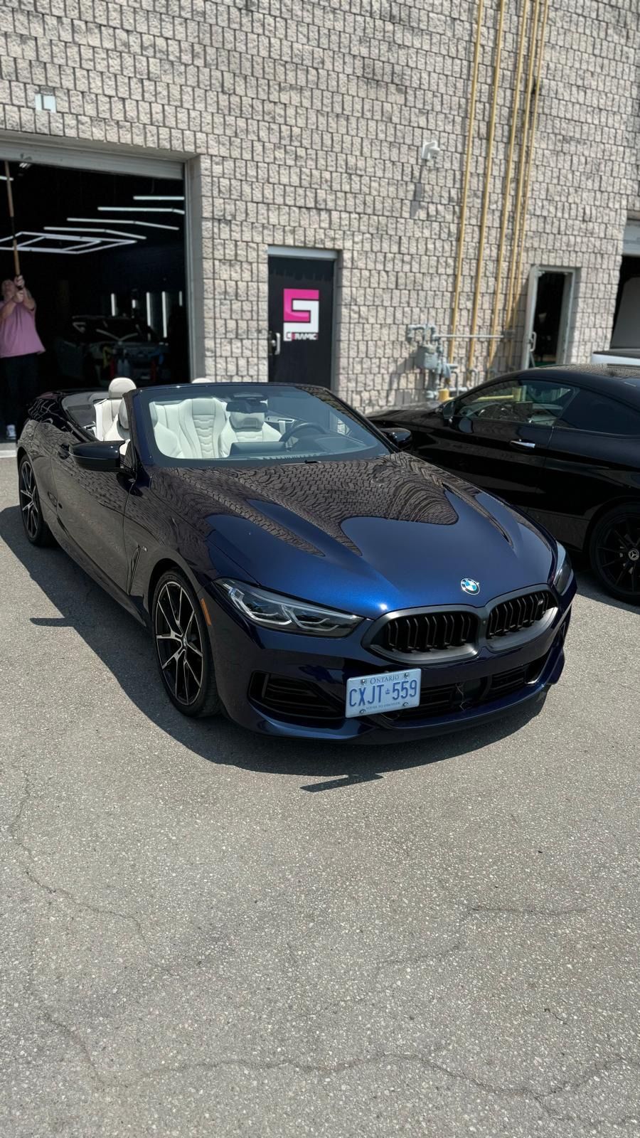 A blue BMW convertible parked on asphalt in front of a stone building with a dark garage entrance.
