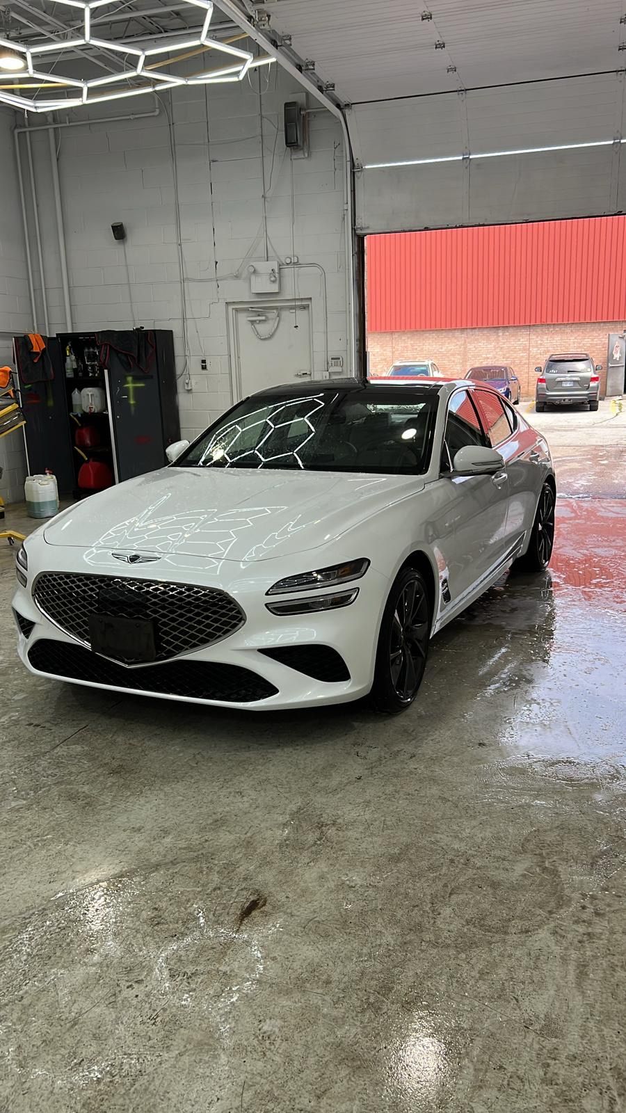 A white Genesis G70 sedan parked in a bright garage with wet, polished floors.