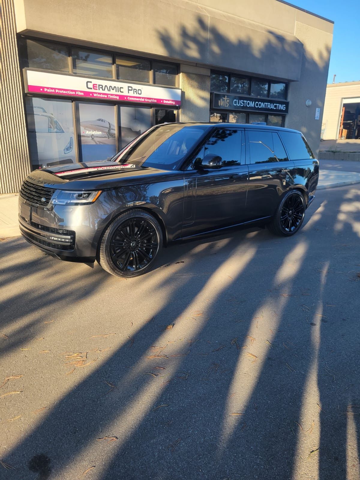 A dark gray Land Rover Range Rover parked in a lot in front of a storefront.