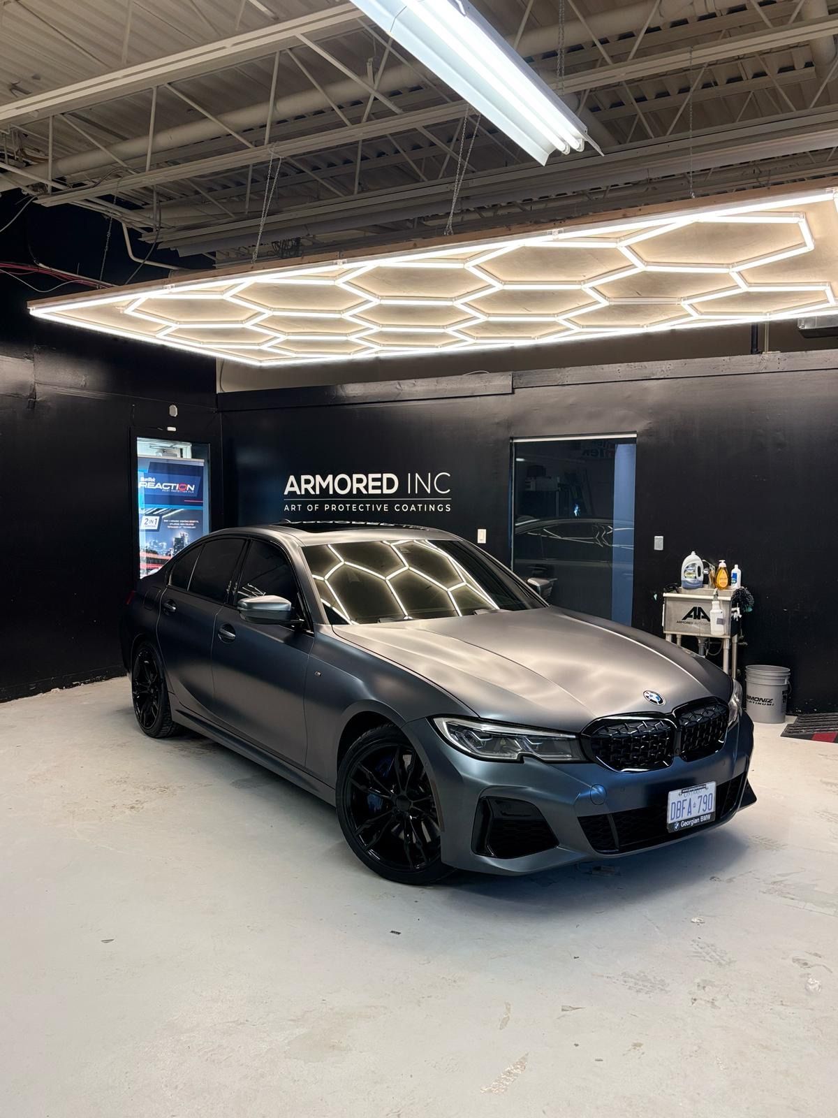 A charcoal gray BMW parked in a garage with black walls and a large, glowing hexagonal LED light fixture on the ceiling.