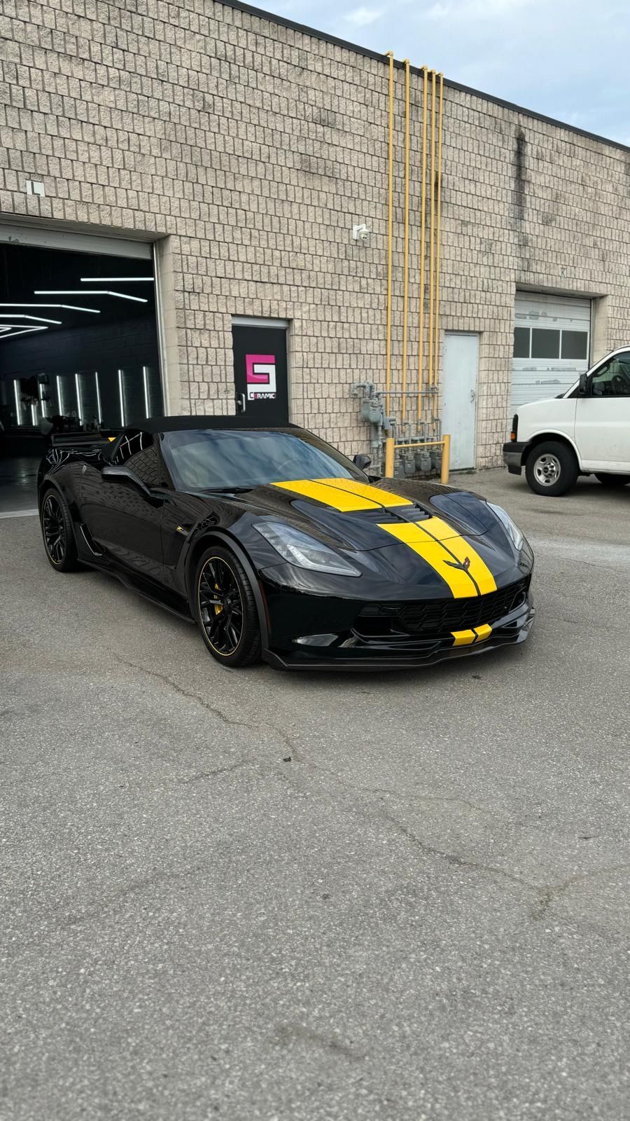A black Chevrolet Corvette with yellow racing stripes parked in front of a stone building.