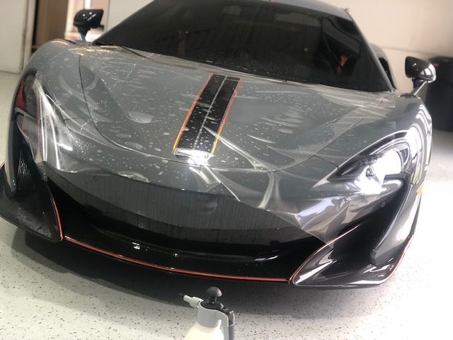 Grey McLaren sports car with protective film being applied.