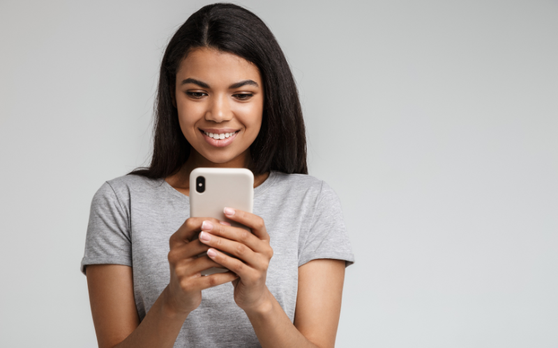 Woman smiling while looking at her phone against a gray background
