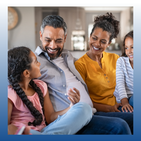 A smiling family sits together on a couch, chatting in a cozy living room.