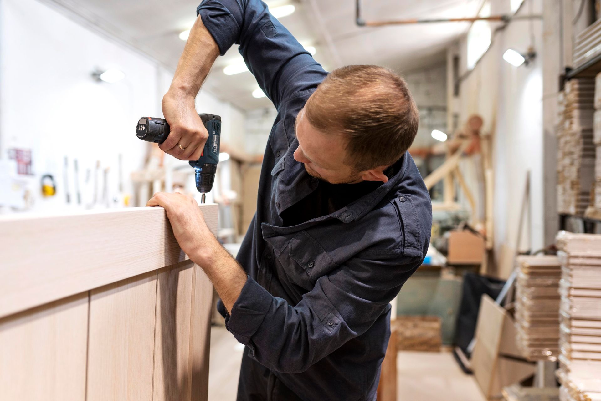 Person using a power drill to assemble wooden panels in a workshop.