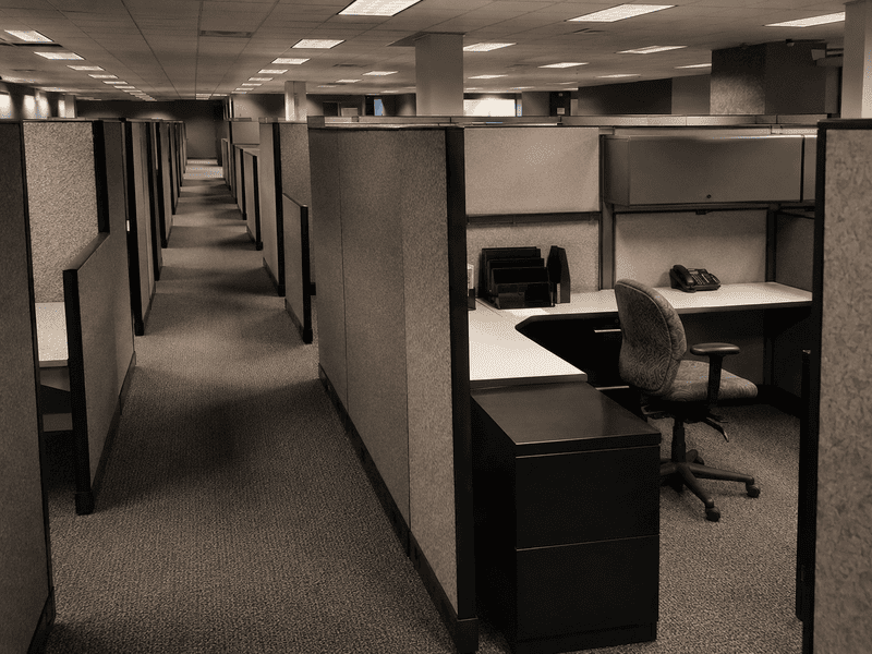 Empty office cubicles with carpeted aisles and fluorescent ceiling lights