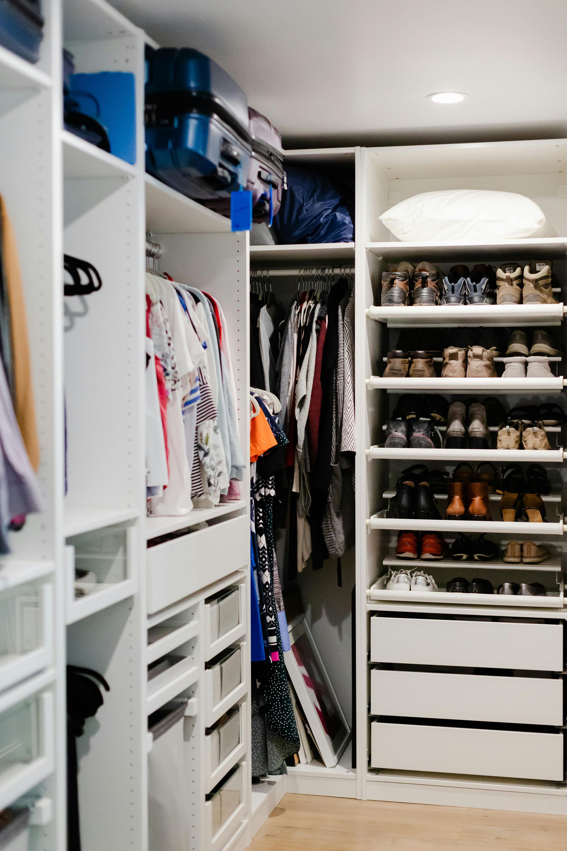 White walk-in closet with clothes, shoes, drawers, and storage on shelves.
