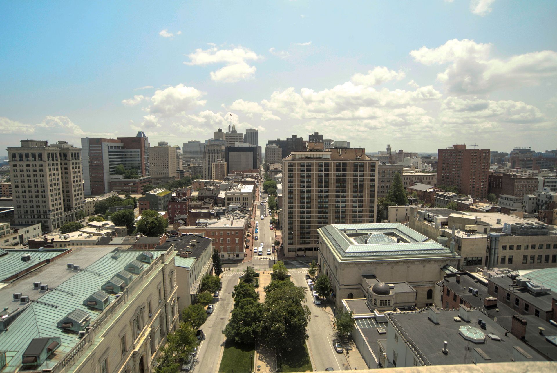 City skyline with mid-rise buildings under a partly cloudy sky, viewed from above.