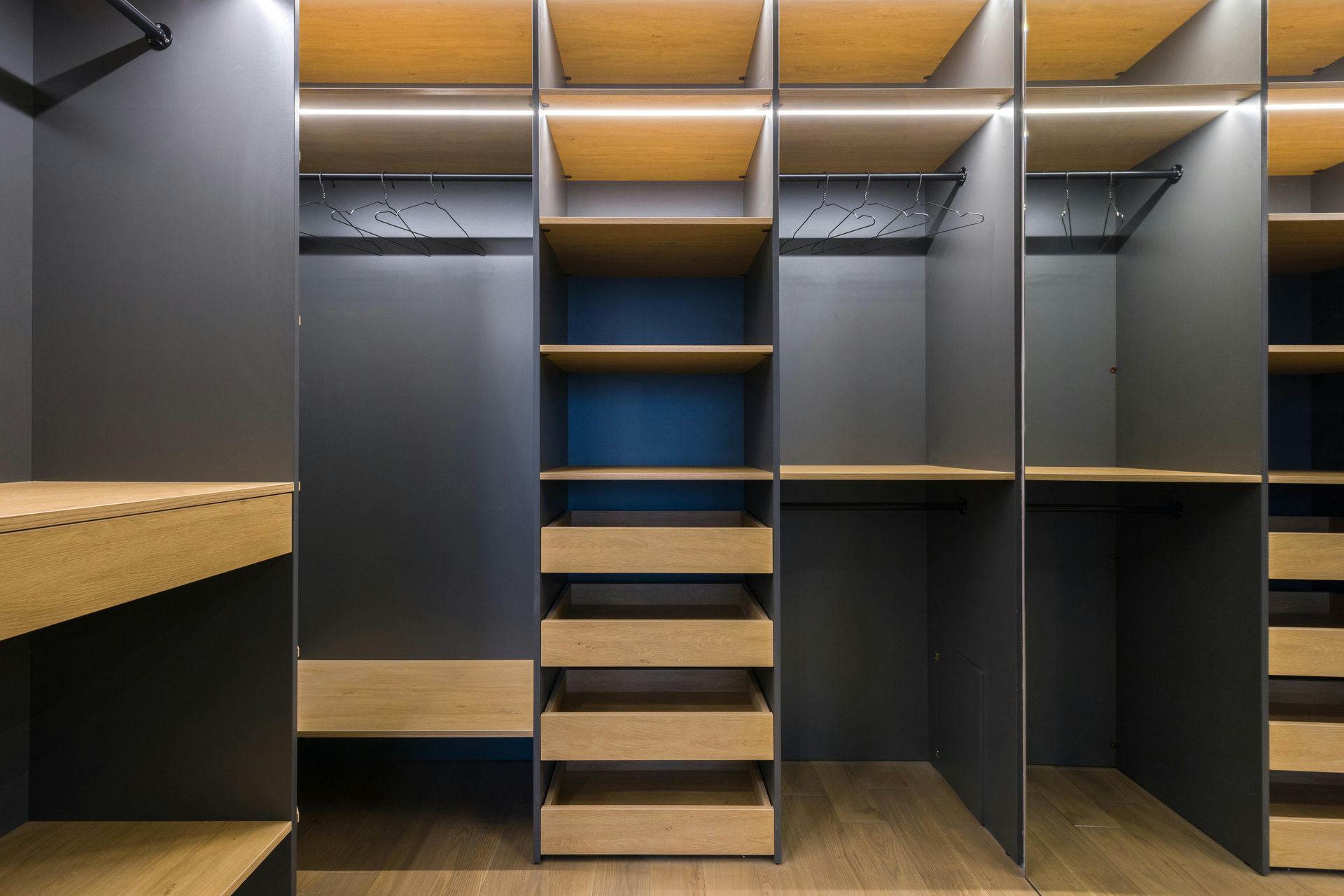 Walk-in closet with dark gray walls, wood shelves, drawers, and hanging rods; lit with warm overhead lighting.