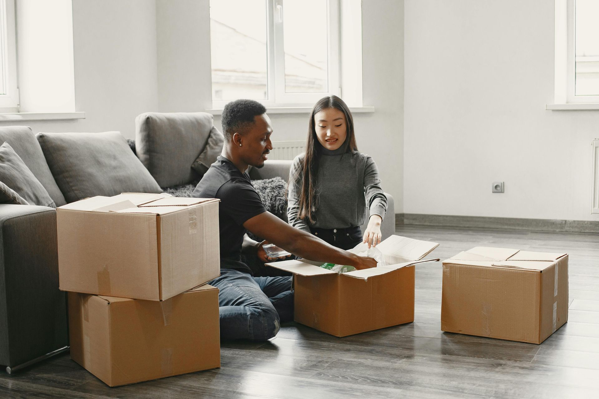 Two people unpacking cardboard boxes in a bright, empty room