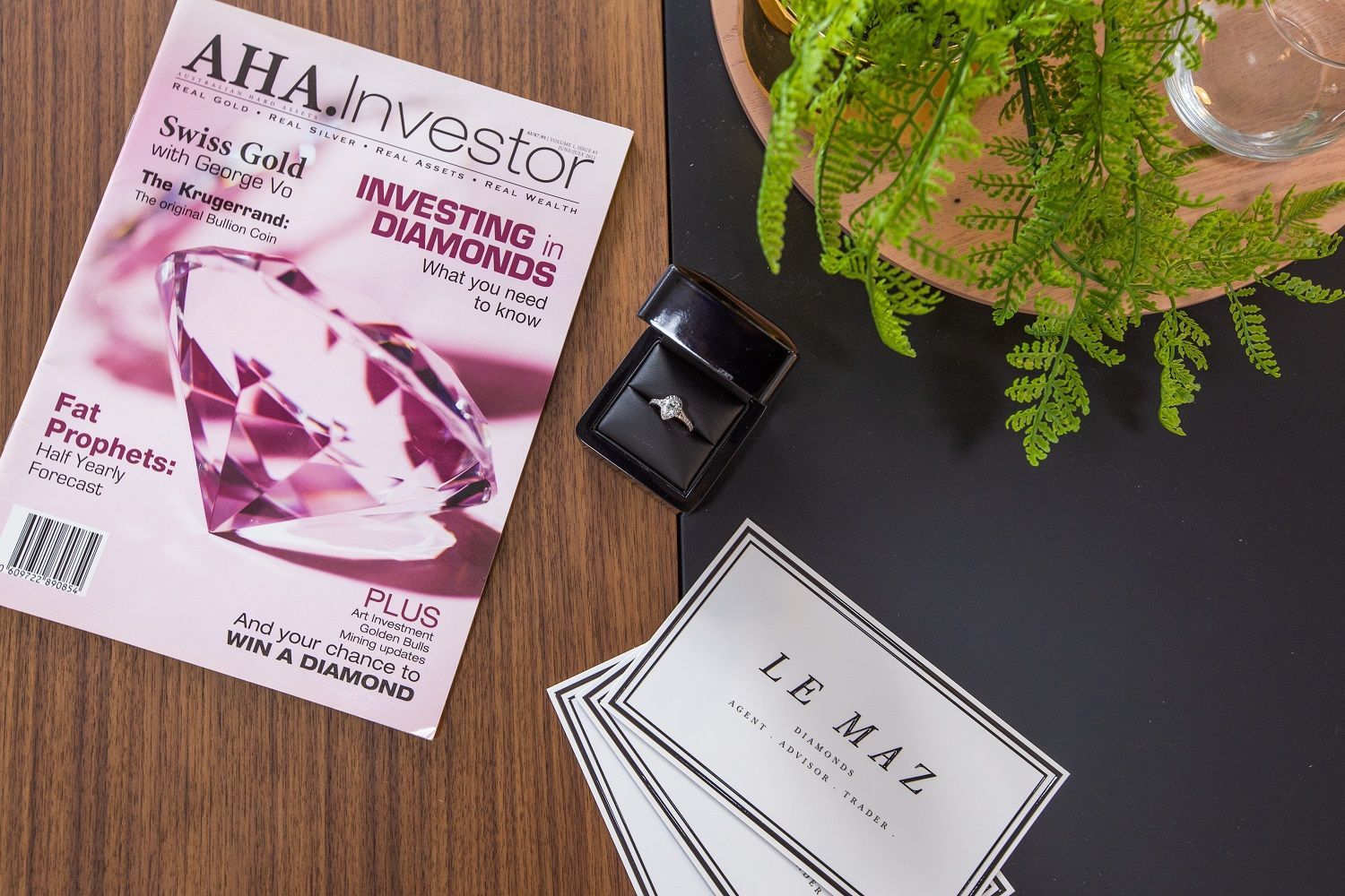 A magazine and a ring are on a table next to a plant.