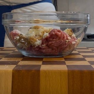 Una ciotola di vetro piena di carne e riso è appoggiata su un tagliere di legno