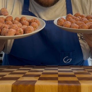 Un uomo con un grembiule tiene in mano due piatti di polpette