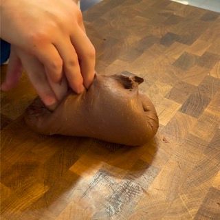 Una persona tiene in mano un pezzo di impasto al cioccolato su un tagliere di legno.