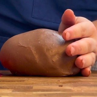 Una persona tiene in mano un oggetto marrone su un tavolo di legno.
