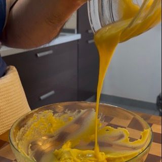 Una persona sta versando del liquido giallo in una ciotola di vetro