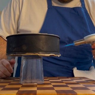 Un uomo con un grembiule sta usando un accendino per accendere una torta
