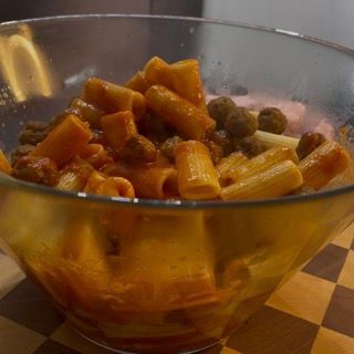 Una ciotola di vetro piena di pasta e polpette su un tavolo a scacchi.