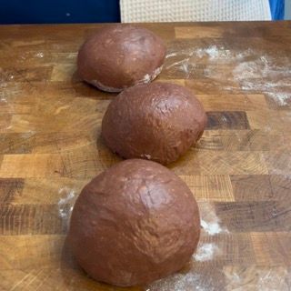 Tre palline di pasta marrone sono appoggiate su un tagliere di legno.