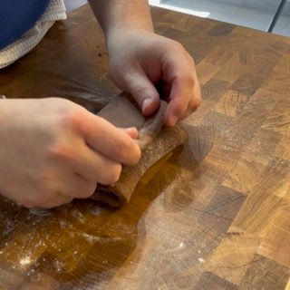 Una persona sta stendendo un pezzo di pasta su un tagliere di legno