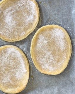 Tre cerchi di pasta ricoperti di zucchero su un pezzo di carta oleata.