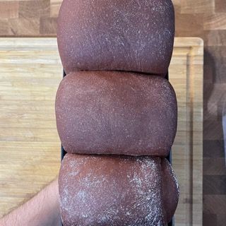 Tre pagnotte di pane al cioccolato sono impilate l'una sull'altra su un tagliere di legno.