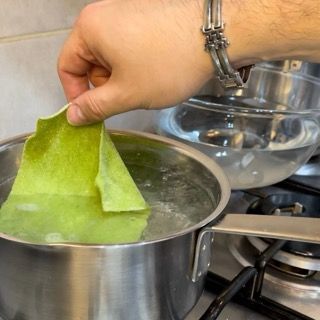 Sfoglie di lasagna verde che cuociono brevemente in acqua bollente.