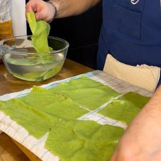 Sfoglie di pasta verde adagiate su uno strofinaccio ad asciugare.