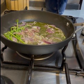 Una padella piena di cipolle e verdure verdi su un fornello