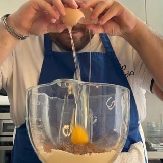 Un uomo con un grembiule sta rompendo un uovo in una tazza graduata