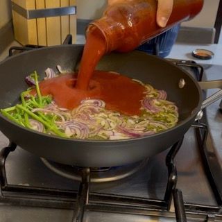 Una persona che versa la salsa di pomodoro in una padella