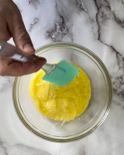 Una persona tiene una spatola sopra una ciotola piena di liquido giallo.
