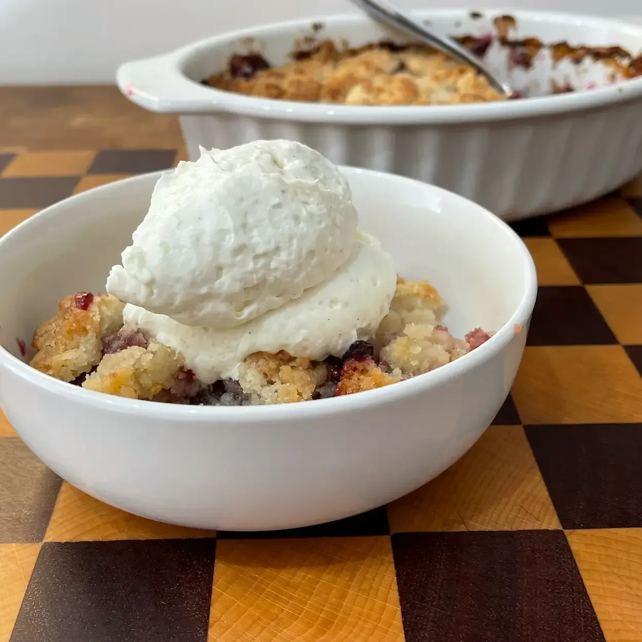 Porzione di crumble ai frutti di bosco servita calda con ganache alla vaniglia. Crumble ai mirtilli e lamponi facile.