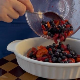 Livellamento dei frutti rossi sul fondo della teglia prima di preparare l'impasto del crumble dolce.