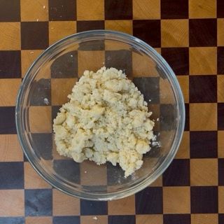 Ciotola con impasto sabbioso e croccante pronto per ricoprire i lamponi nel crumble ai frutti di bosco.