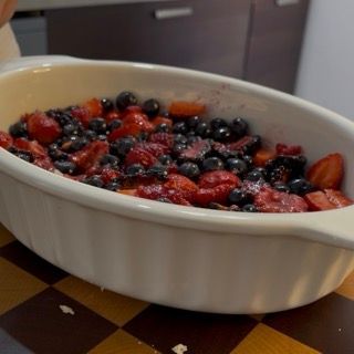 Distribuzione uniforme delle grosse briciole di frolla sopra la frutta per il crumble ai frutti rossi in teglia.
