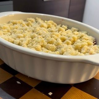 Pirofila di crumble ai mirtilli e lamponi interamente ricoperta di impasto, pronta per la cottura in forno.