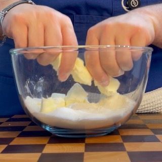 Lavorazione manuale degli ingredienti sbriciolando il burro freddo per il crumble ai frutti di bosco.