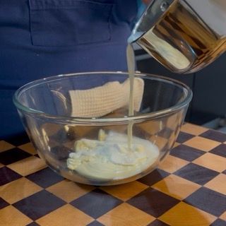 Aggiunta del primo terzo di panna calda al cioccolato bianco per la ganache del crumble ai frutti di bosco.