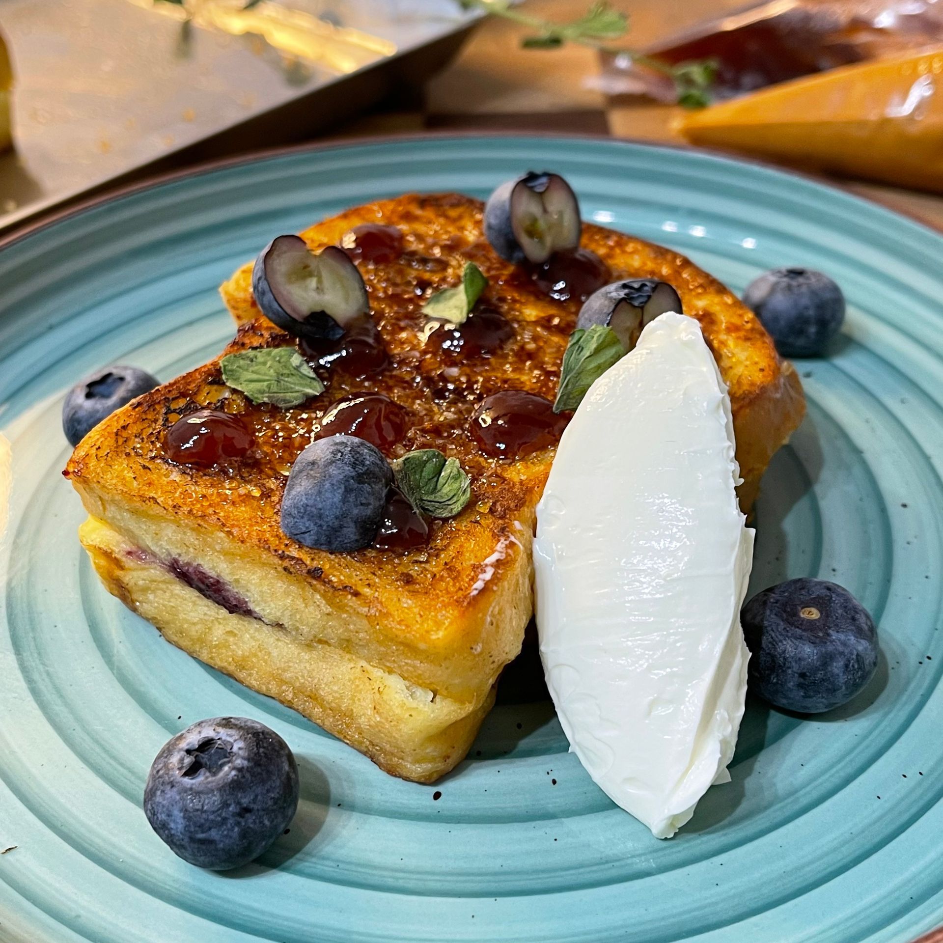 Una fetta di french toast con mirtilli e panna montata su un piatto blu.