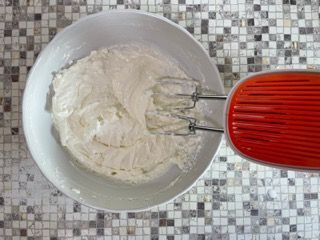 Una ciotola di panna montata accanto a una planetaria su un bancone piastrellato.